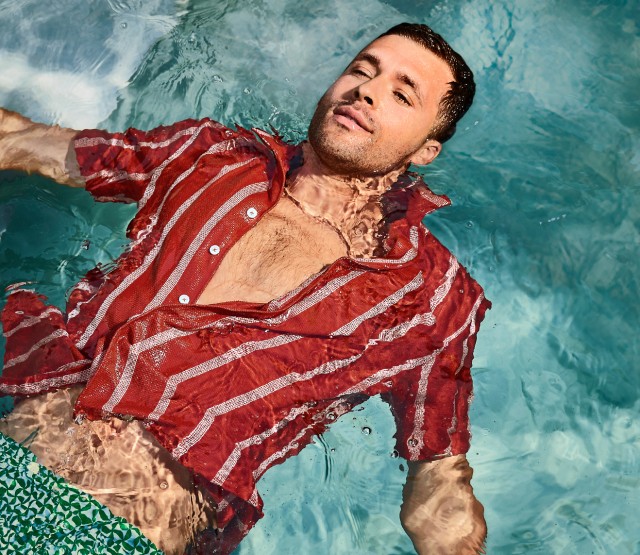 Auf dem Bild ist eine Person zu sehen, die entspannt in einem Pool schwimmt, gekleidet in ein rot-weiß gestreiftes Hemd und grüne gemusterte Shorts.