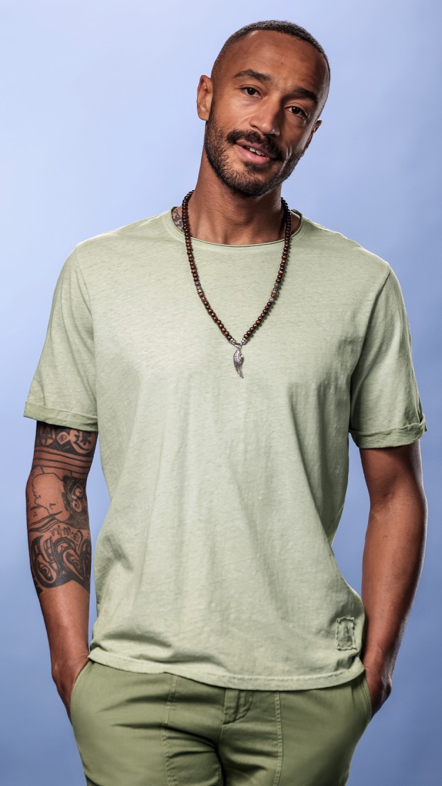 Ein Mann trägt ein natürgrünfarbenes T-Shirt mit einer Holzekette.