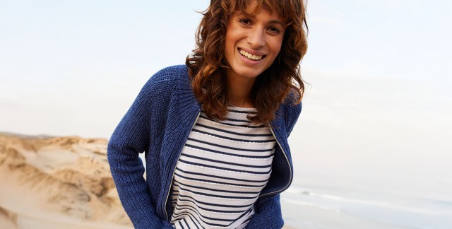 Frau in gestreifetem Oberteil und blauer Strickjacke an der Küste