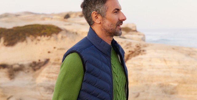 Mann in grünem Pullover und blauer Weste an der Küste