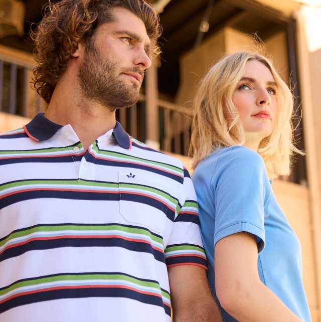 Mann mit gestreiftem Polo und Frau mit blauem Polo stehen vor einer Häuserfront