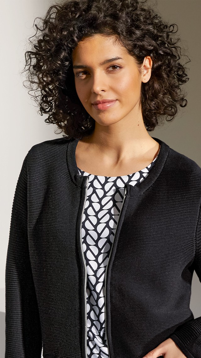 Eine Dame mit einer schwarzen Reißverschlussjacke und einer schwarz weißen Bluse darunter