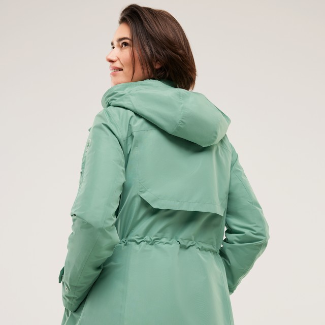 Eine Frau trägt eine grüne Jacke und schaut nach hinten 