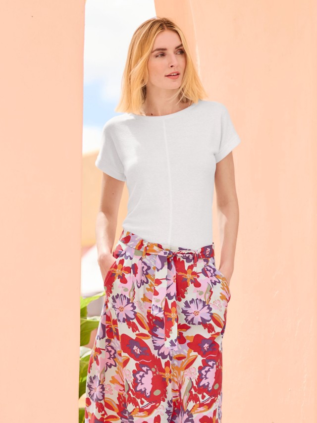 Eine sommerlich gekleidete Frau trägt ein weißes Leinenmixshirt und einen luftigen Midirock mit floralen Muster.