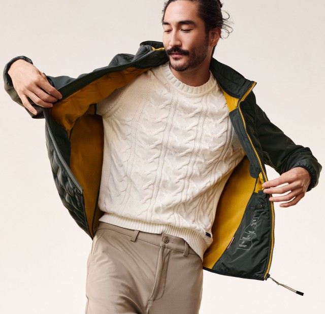 Mann in einer schwungvollen Pose hält seine Jacke auf und schaut nach unten. 