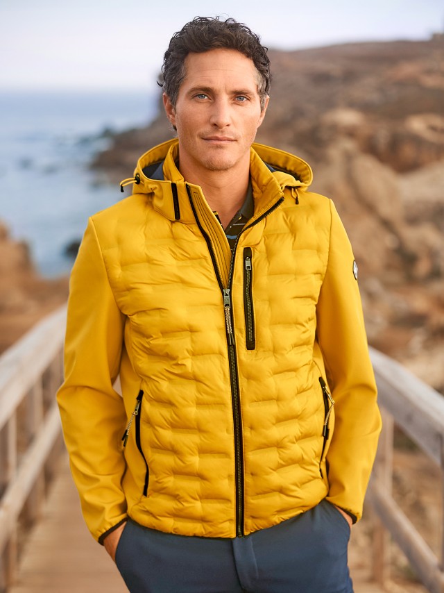 Mann am Strand trägt eine gelbe Jacke mit Klimakammern und schaut in die Kamera