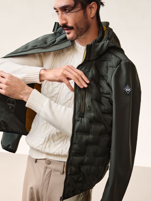 Ein Mann trägt einen olivfarbenen Blouson, darunter einen hellen Strickpullover.