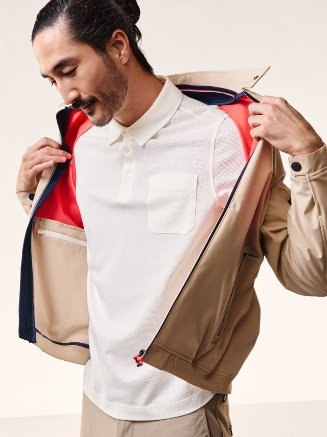 Ein Mann trägt ein Polo-Shirt und öffnet sein Blouson. 