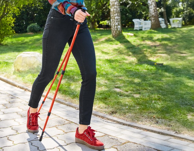 Frau mit Trekkingstöcke im Outdoor-Look in einer sommerlichen Umgebung.