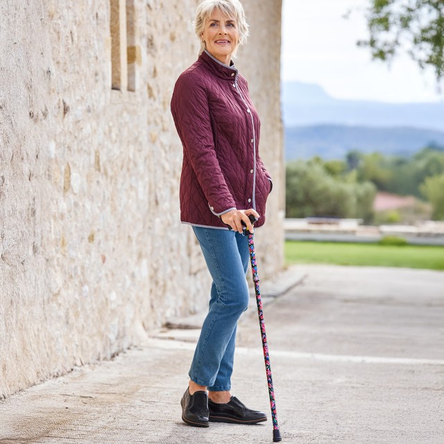 Frau mit einer Geh-Hilfe im frühlingshafter Landschaft.