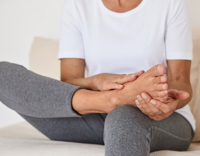 Eine sitzende Frau hält Ihren Fuß in den Händen