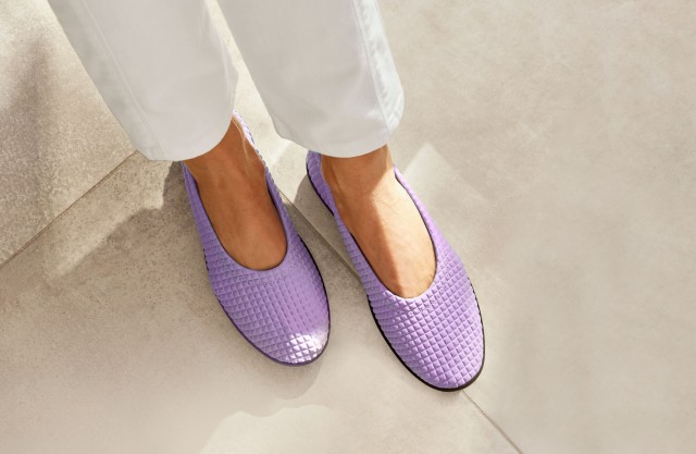 Damenbeine in weißer Hose trägt fliederfarbene Hallux-Slipper.