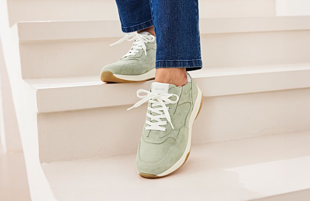 Damenbeine mit blauer Jeans tragen ein mintfarbenes Sneakerpaar.