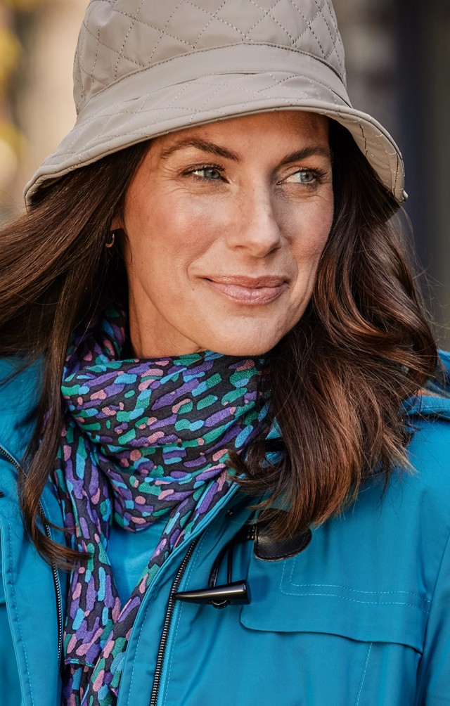 Frau trägt eine wasserdichte Regenjacke mit einem bunten Tuch und dazu einen Regenhut.